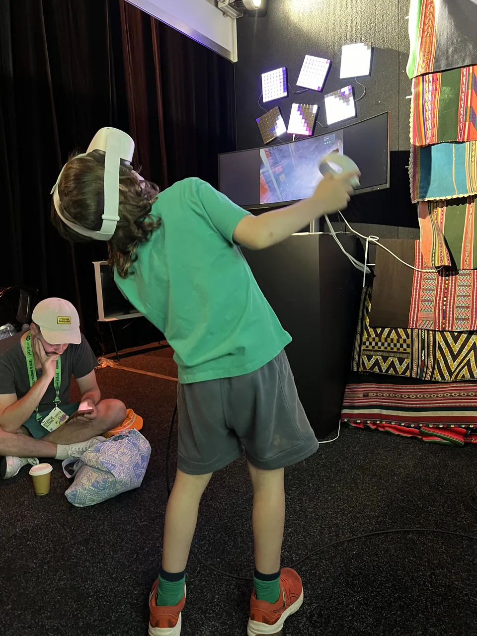 Un niño con un visor de realidad virtual estira la mano, mientras otro niño está sentado en el suelo.