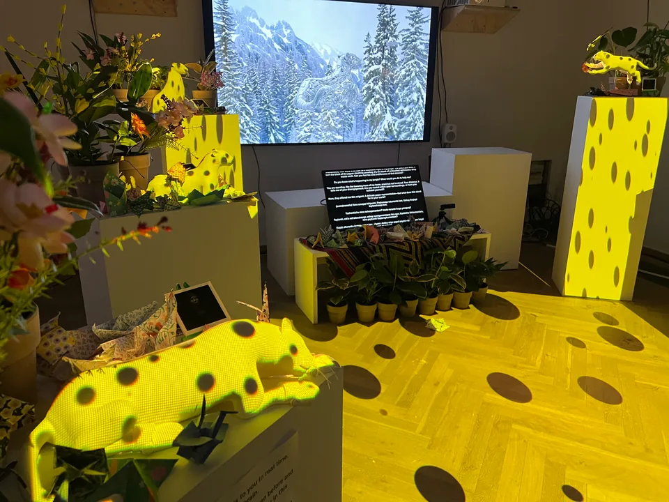 A gallery lit in yellow with dark spots: white jaguars lie on plinths among orchids, paper cranes and plants, before a screen of a snowy forest.