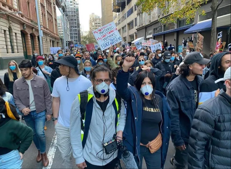 Una multitud marcha por una calle de Sídney, muchas personas con barbijo.