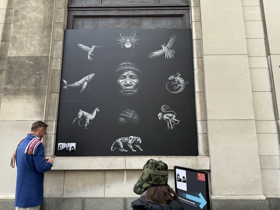 Un gran panel negro con animales plateados alrededor del rostro de una abuela, sobre un edificio de piedra. Un hombre lo mira.
