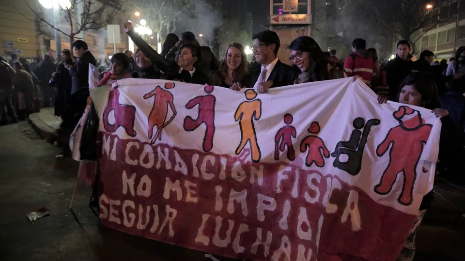 Manifestantes de noche sostienen una pancarta: mi condición física no me impide luchar.