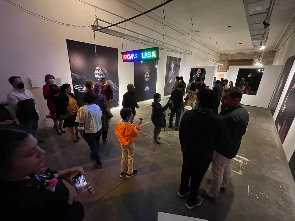 Visitantes llenan una galería con grandes retratos en blanco y negro, bajo un letrero luminoso que dice Las Awichas.