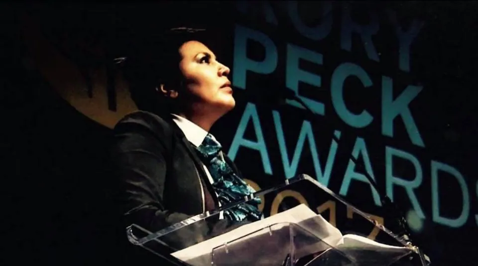 Una mujer en un atril, frente al telón de fondo de los Rory Peck Awards.