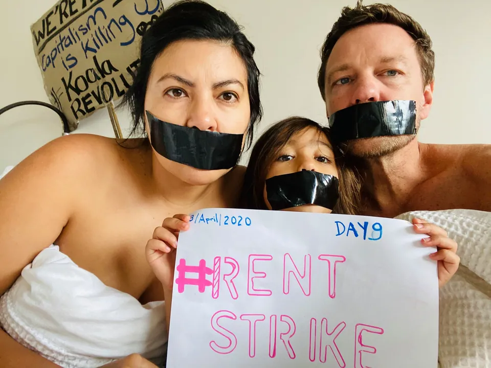 Una familia con cinta sobre la boca sostiene un cartel: Rent strike, day 9.