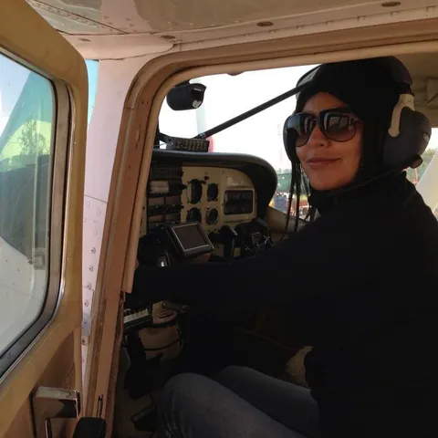 Una mujer con lentes de sol y audífonos a los mandos de una avioneta.