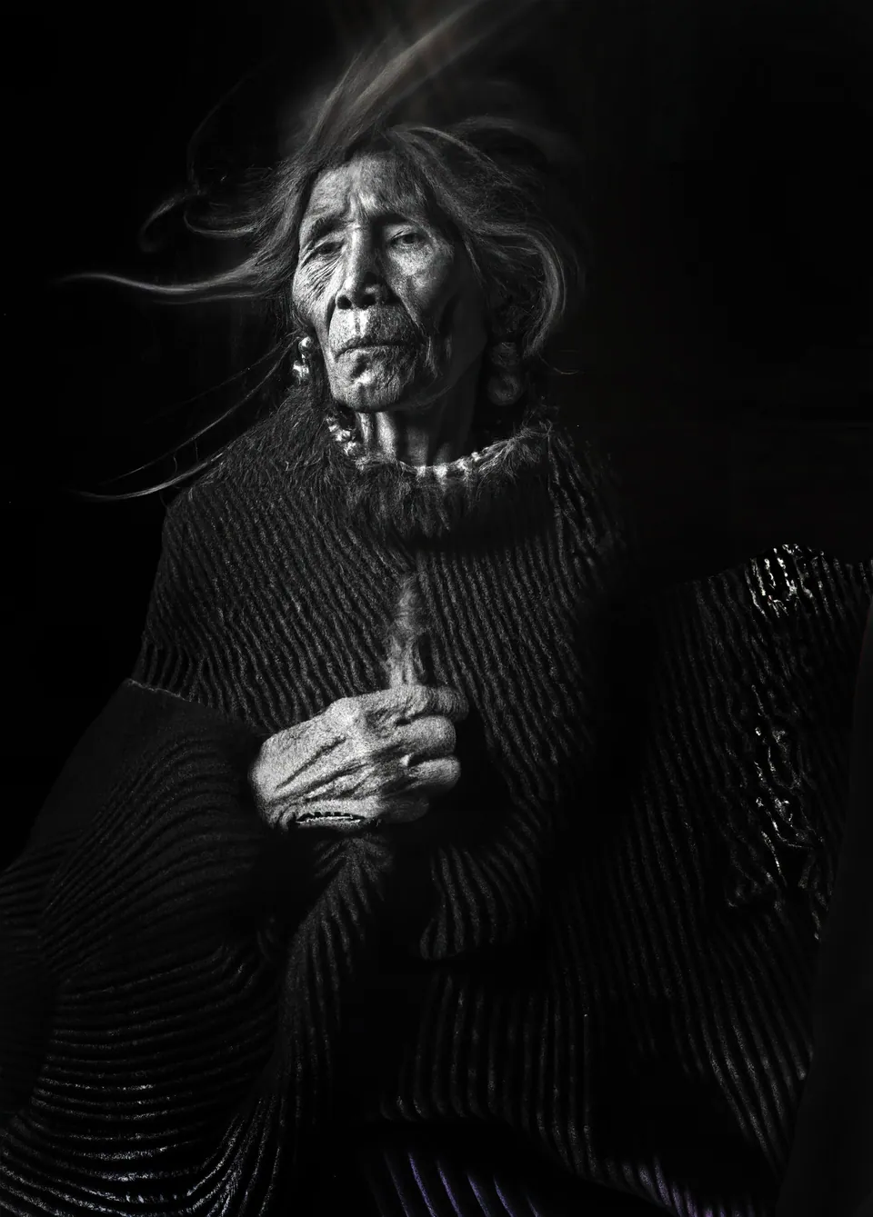 Un retrato hecho con IA, en blanco y negro: una anciana andina, con el cabello levantado por el viento.