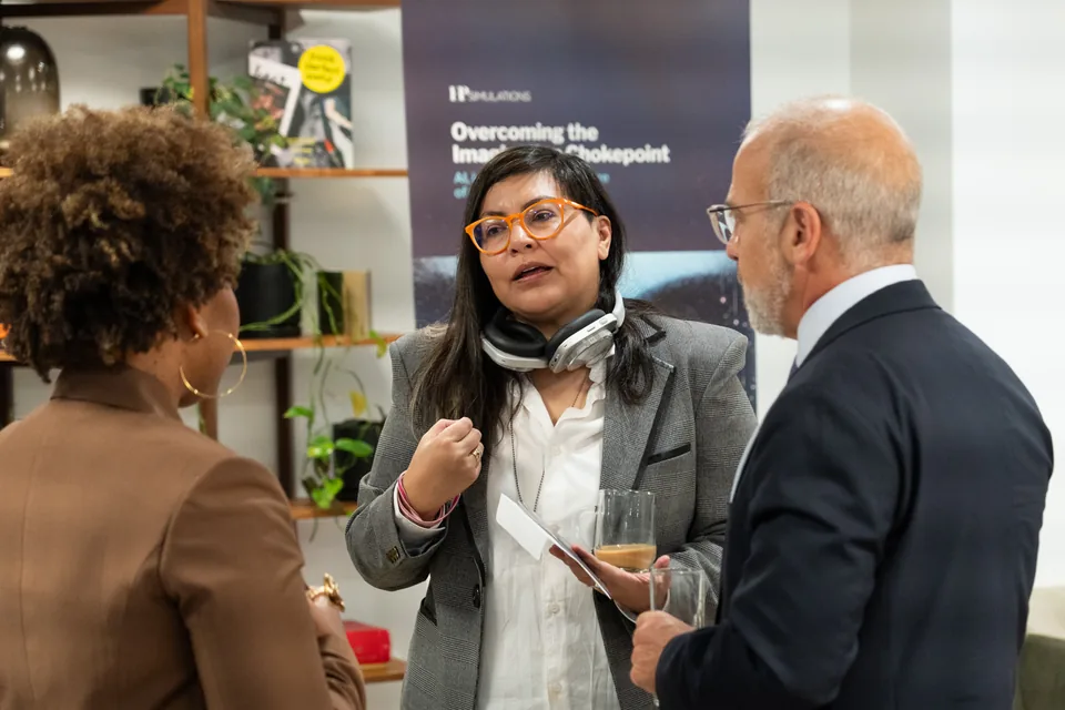 Tres personas conversan frente a un banner que dice Overcoming the Imagination Chokepoint.