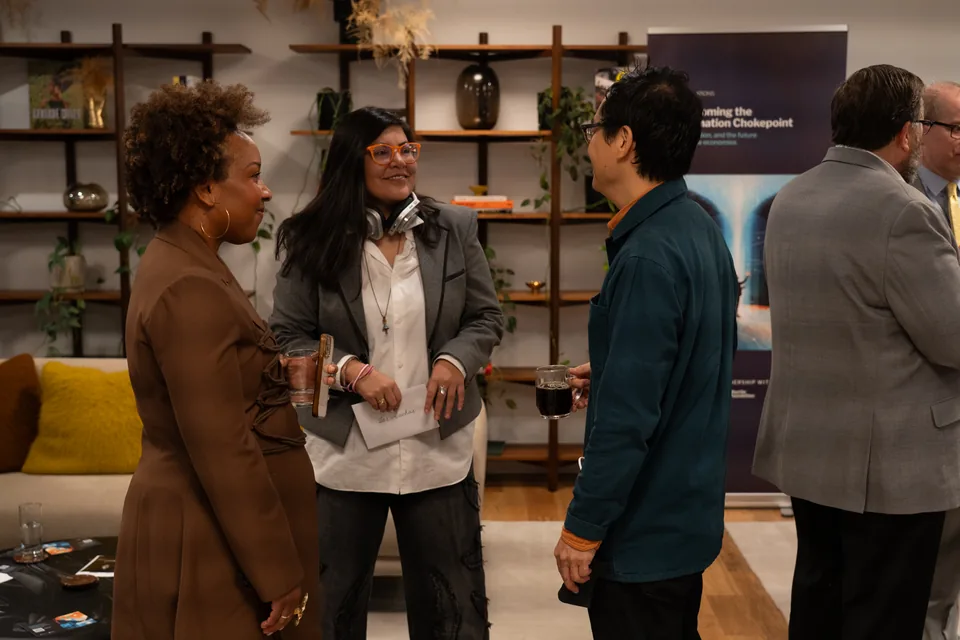 Tres personas conversan tomando café junto al banner de la simulación; una sostiene un sobre que dice Las Awichas.