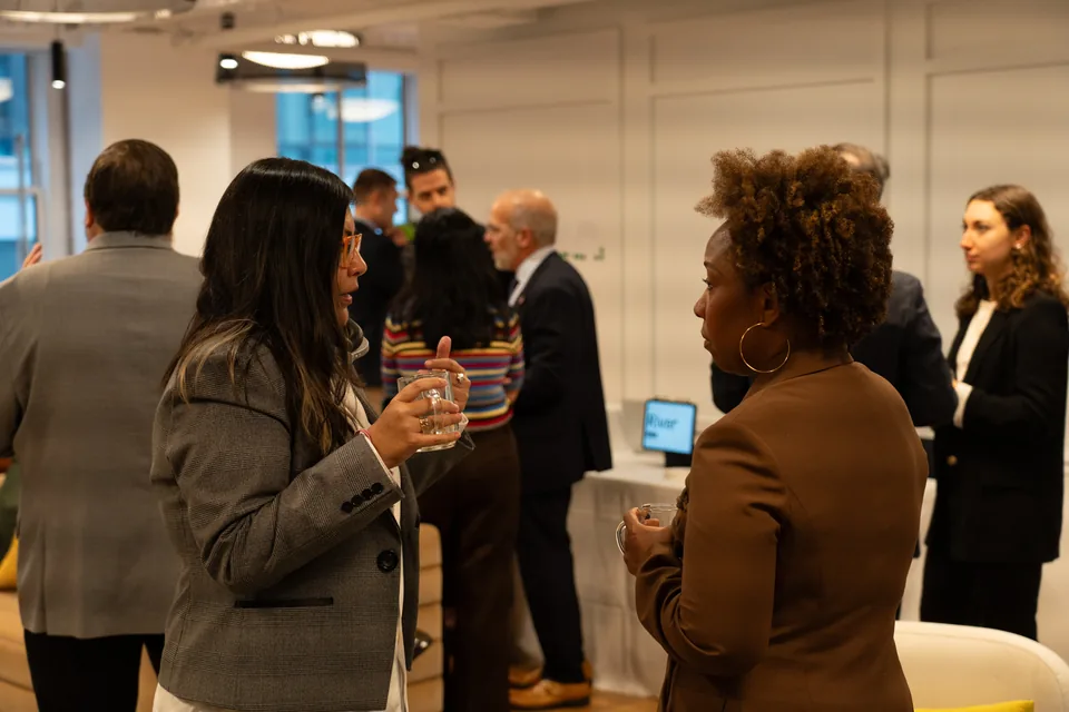 Dos mujeres conversan entre los invitados en una sala luminosa.